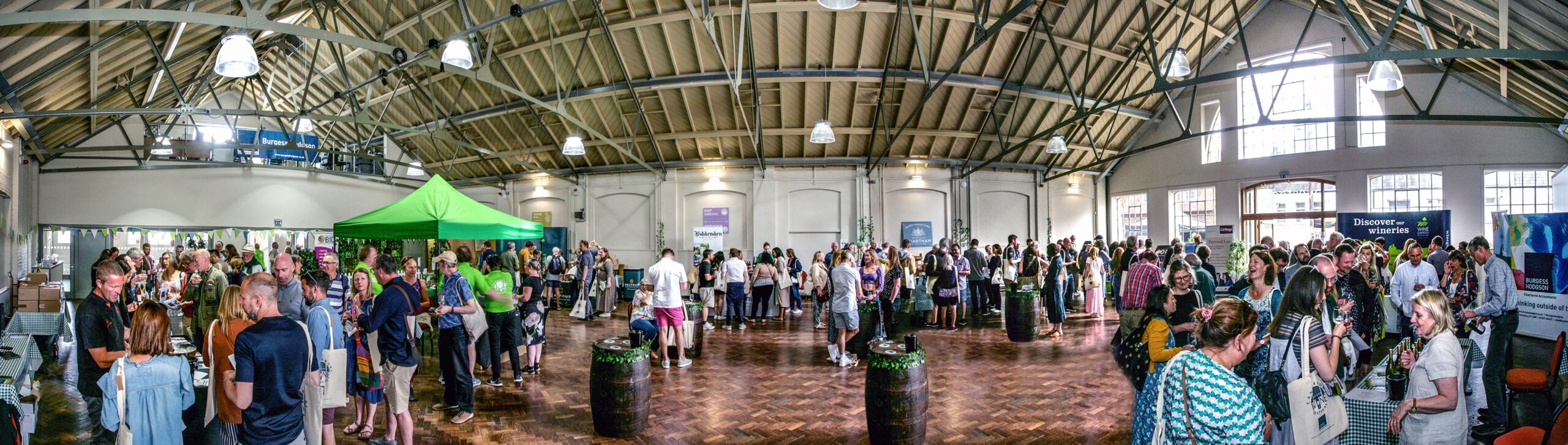 A panoramic photo of a people at a wine festival with vineyard stands and people tasting wine at Westgate Hall.