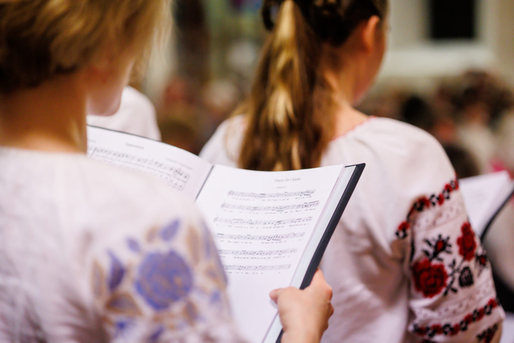 Women in white tops reading choir music